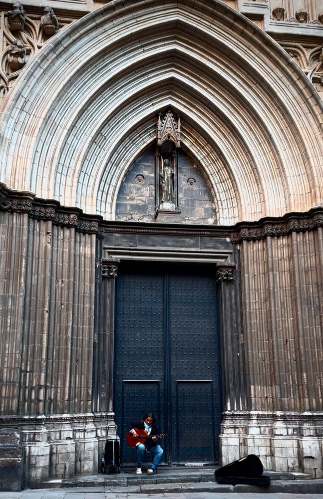 A lone guitar player sits in front of a large cathedral door in a Gothic Quarter alleyway in Barcelona