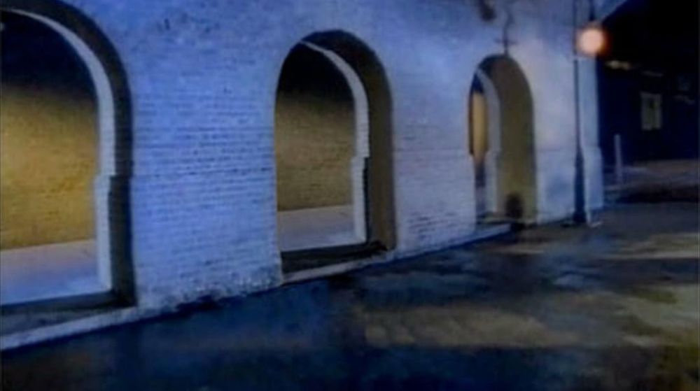 A street at night with brick arches along the side and a street lamp. It’s the bridge underpass or whatever from the “Never Gonna Give You Up” music video. 