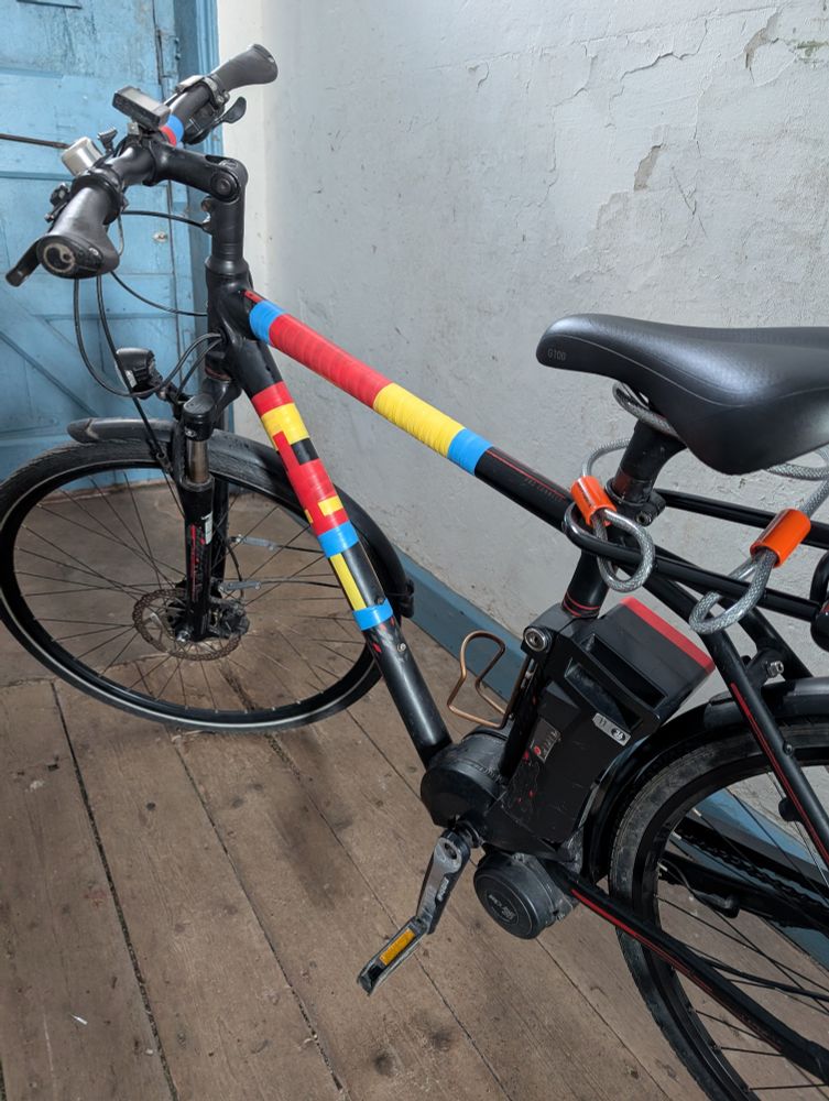 A black bicycle being decorated with brightly coloured tape in red, yellow and blue
