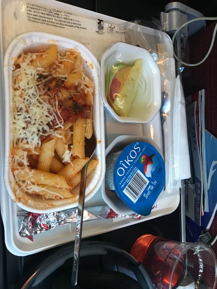 sideways photo of penne pasta with tomato ans parmesan, plus yogurt and fruits and a drink. airport meal