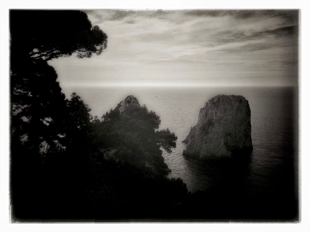 a image of mine that reminds me of the deep yearning in caspar david friedrich’s ‘sehnsuchtslandschaften, where the visible is but a veil over the infinite. the jagged rocks rise from the sea like forgotten thoughts of the earth, solitary and eternal, bearing the weight of time. the silhouetted trees bent and reaching, evoke the tender asymmetry of a hasegawa tōhaku pine, their presence both framing and dissolving the scene.

here, the horizon breathes a thin line where sky and water converse in whispers. the scene is not one of drama, but of quiet revelation. nature is not a backdrop for man’s striving, but a mirror to his interiority: longing, impermanence, acceptance.

as in shinkei’s ink landscapes, mist and emptiness are as vital as form. the photograph resembles this: the open sea is a vastness that invites both melancholy and liberation.

In the spirit of romanticism, the viewer is not outside this scene but absorbed by it. the rocks do not merely stand in the sea; they are metaphors of solitude and the sublime indifference of nature. the trees do not simply frame the image; they suggest the ephemeral nature of vision, the partiality of human grasp.