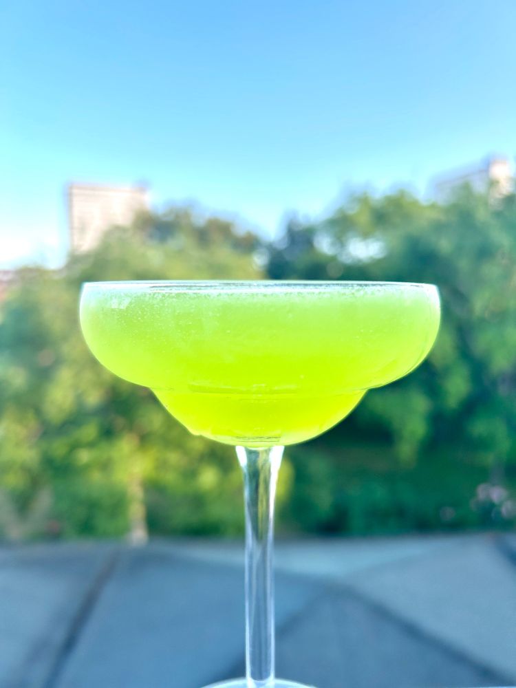 A lime green cocktail against an urban garden background the roofs and trees are out of focus.