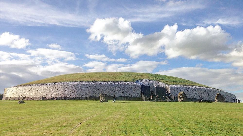Newgrange passage tomb: A round structure in a field, with white stone walls and grass on top.