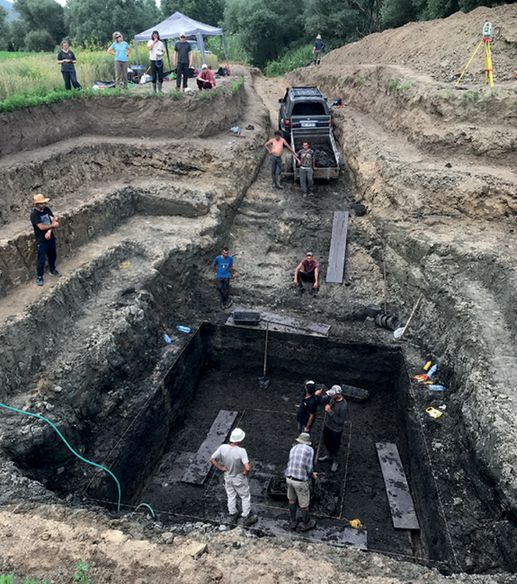 Several archaeologists excavating in a square pit with several terraced layers. 