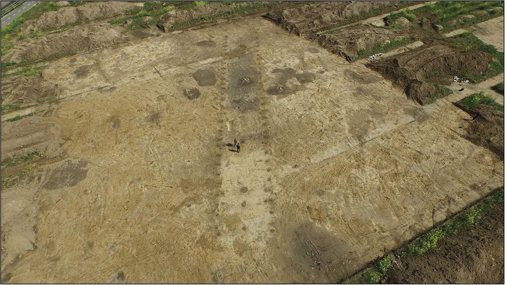 Outline of a long building from above, defined by many post-holes along the walls. Two people stand in the outline for scale.