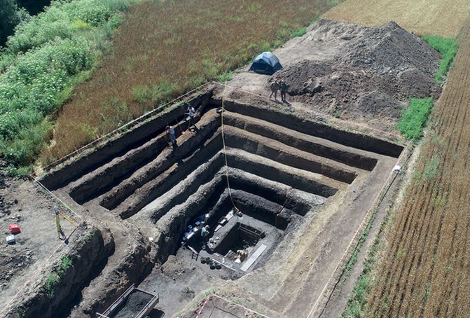 Oblique aerial view of a square, tiered excavation.