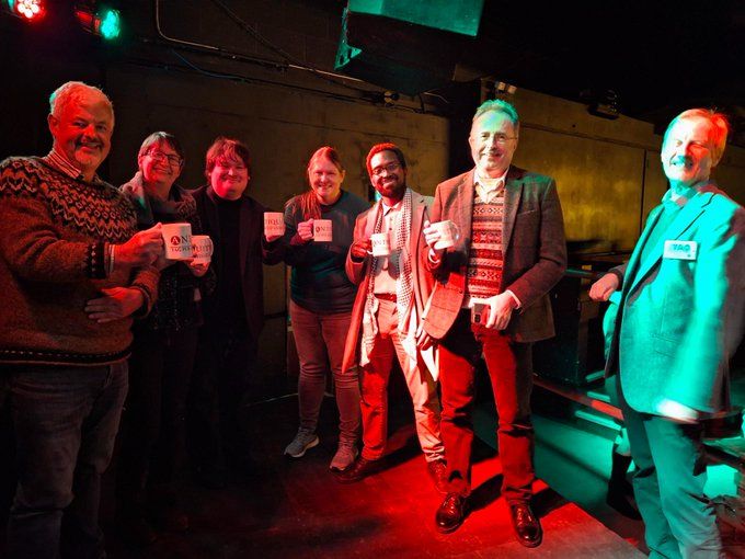A team of six people smiling and holding Antiquity mugs. Incoming Antiquity Editor Prof. Robin Skeates stands next to them smiling.
