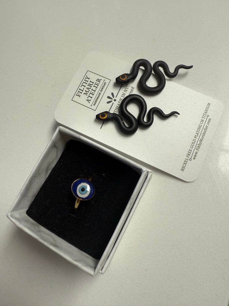 An evil eye ring with gold band and polymer clay black snake earrings with gold crescent moon on the heads. 