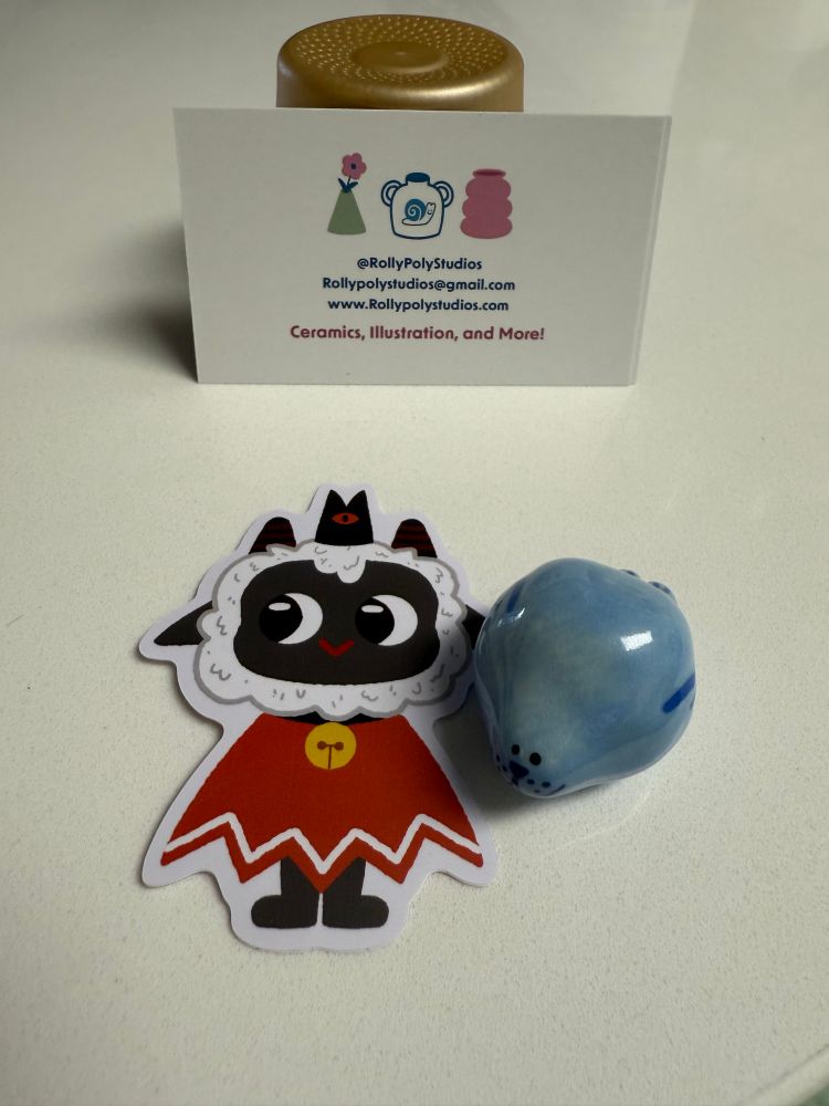 Sticker of the cult leader from Cult of the Lamb and a tiny ceramic hand painted chunky round seal. 