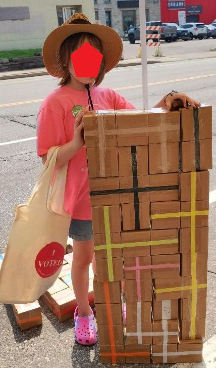Young lady with face obscured by a red pentagon standing next a tiling puzzle she made.