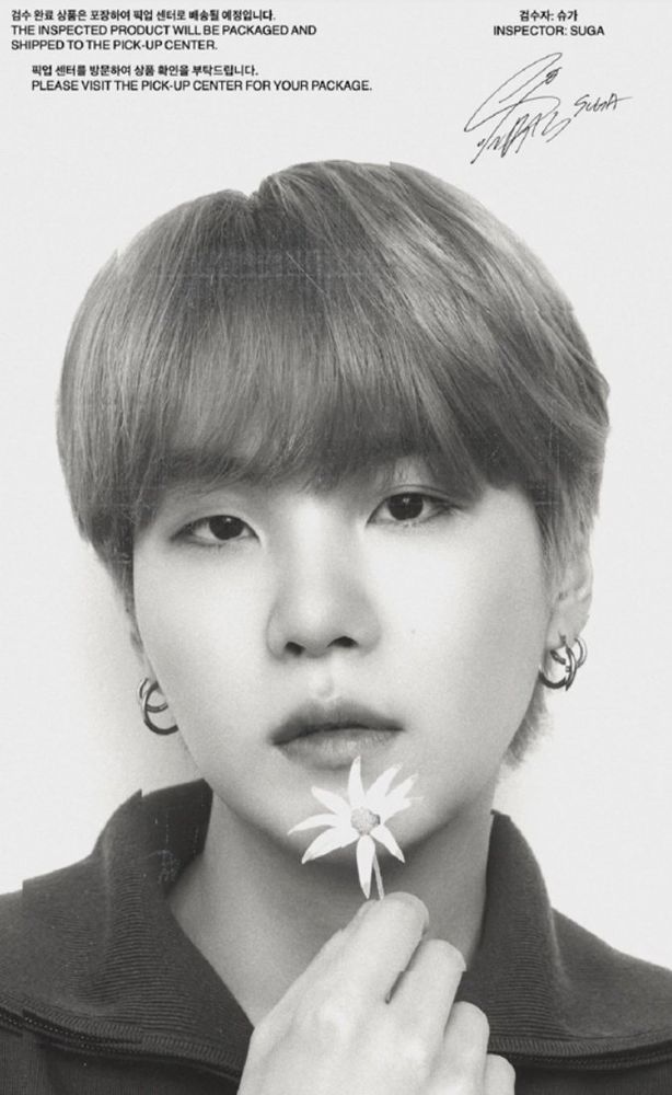 Nesta imagem em preto e branco, vemos Yoongi segurando uma flor de pétalas brancas e olhando para a frente com um semblante levemente sério. Ele está com o cabelo curto e claro e está vestindo uma roupa escura. Além disso, está usando um par de brincos de argola.

In this black and white image, we see Yoongi holding a white flower and looking straight ahead with a slightly serious expression. He has short, light hair and is wearing a dark outfit. He is also wearing a pair of ring earrings.