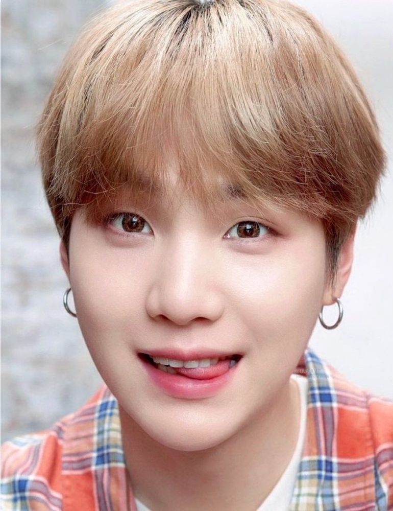 Yoongi está olhando para frente com uma expressão engraçada e mordendo levemente a própria língua. Ele está com o cabelo castanho claro quase loiro, vestindo uma blusa xadrez e com um par de brincos de argola.

Yoongi is looking straight ahead with a funny expression and slightly biting his tongue. He has light brown, almost blond hair and is wearing a plaid shirt and a pair of ring earrings.