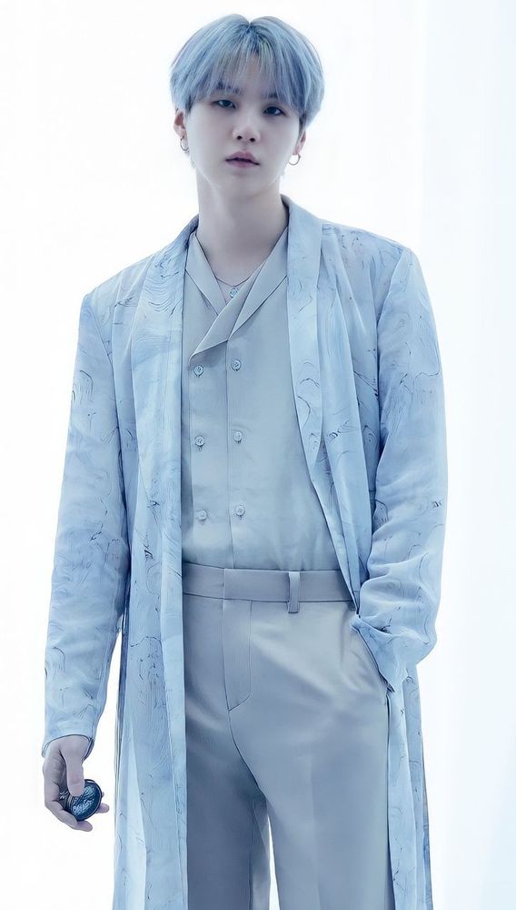 Yoongi está olhando para frente e usando um conjunto de roupas claras, assim combinando com o seu cabelo branco acinzentado. O fundo do estúdio também está branco.

Yoongi is looking straight ahead and wearing a light-colored set of clothes, which matches his grayish-white hair. The studio background is also white.