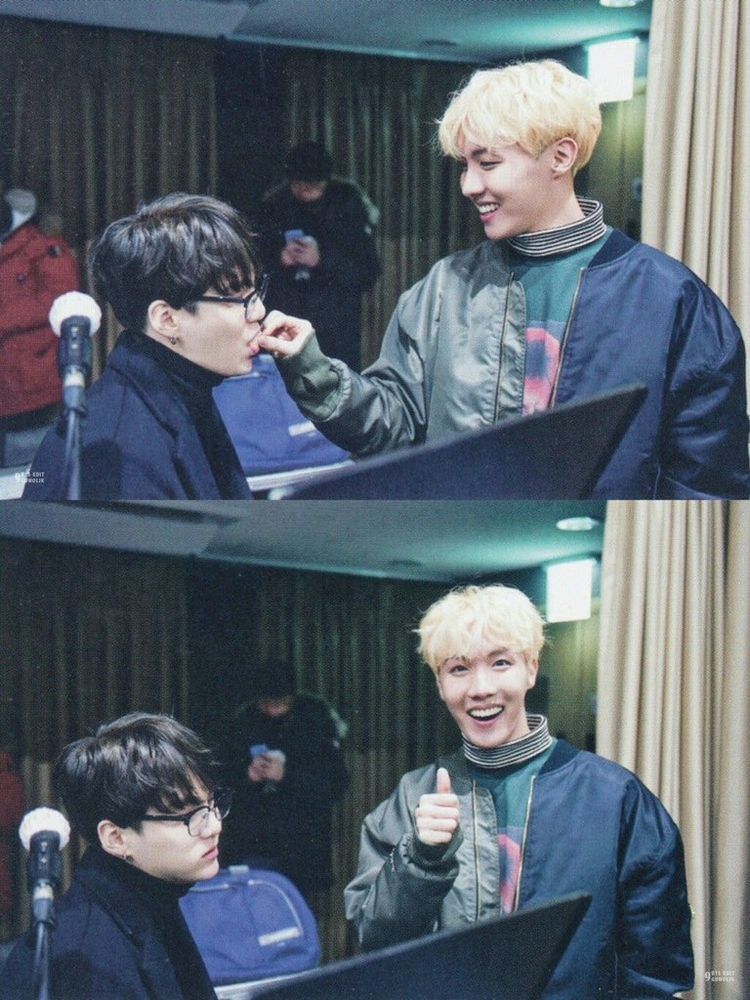 Hoseok o que está de pé e ali e dá um alimento na boca do Yoongi, que está segurando o riso enquanto está sentado. Depois ele sorri para a câmera e dá um joinha. O BTS estava em um estúdio de gravação nesse dia.

Hoseok is the one standing there and feeding Yoongi, who is holding back laughter while sitting down. He then smiles at the camera and gives a thumbs up. BTS was in a recording studio that day.