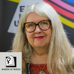 A picture of a smiling Josie Moon. She has long grey hair, is wearing tortoise-shell spectacles and a red jumper