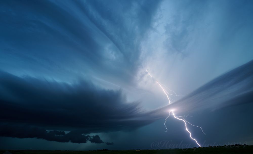 A deep blue structured supercell throws bolts out of the top. The silhouette of the plains is just visible at the horizon.
