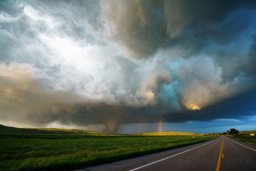 The lush green Nebraska sandhills fill the foreground on either side of the 2 lane highway I’m driving down. In front of me, a thunderstorm beautifully lit by the setting sun, and underneath it a massive violent tornado accompanied by a rainbow. The sun partially peaking through the clouds creates incredible lighting and contrast in this scene with the shadows really accentuating the depth of the storm. The way the tornado is lit right next to the rainbow gives beauty to an incredibly destructive force.