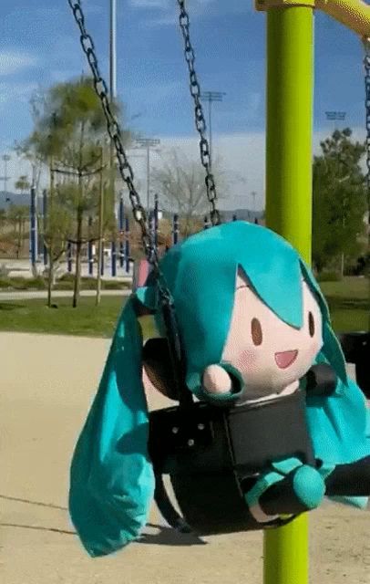 a stuffed hatsune miku sitting on a swing in a park