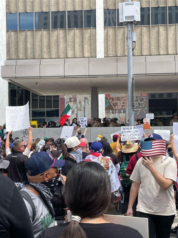 Crowd of protesters in front of LA Federal Building. On the front plaza protesters stand face to face with National Guard. Signs say “ICE out of LA” and “When injustice becomes law, resistance becomes duty.”