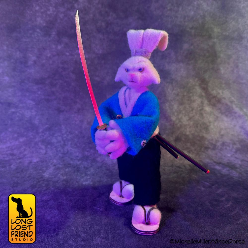 Completed Usagi Yojimbo needle felted figure, posed in a battle stance, holding katana in two-handed grip, looking intense