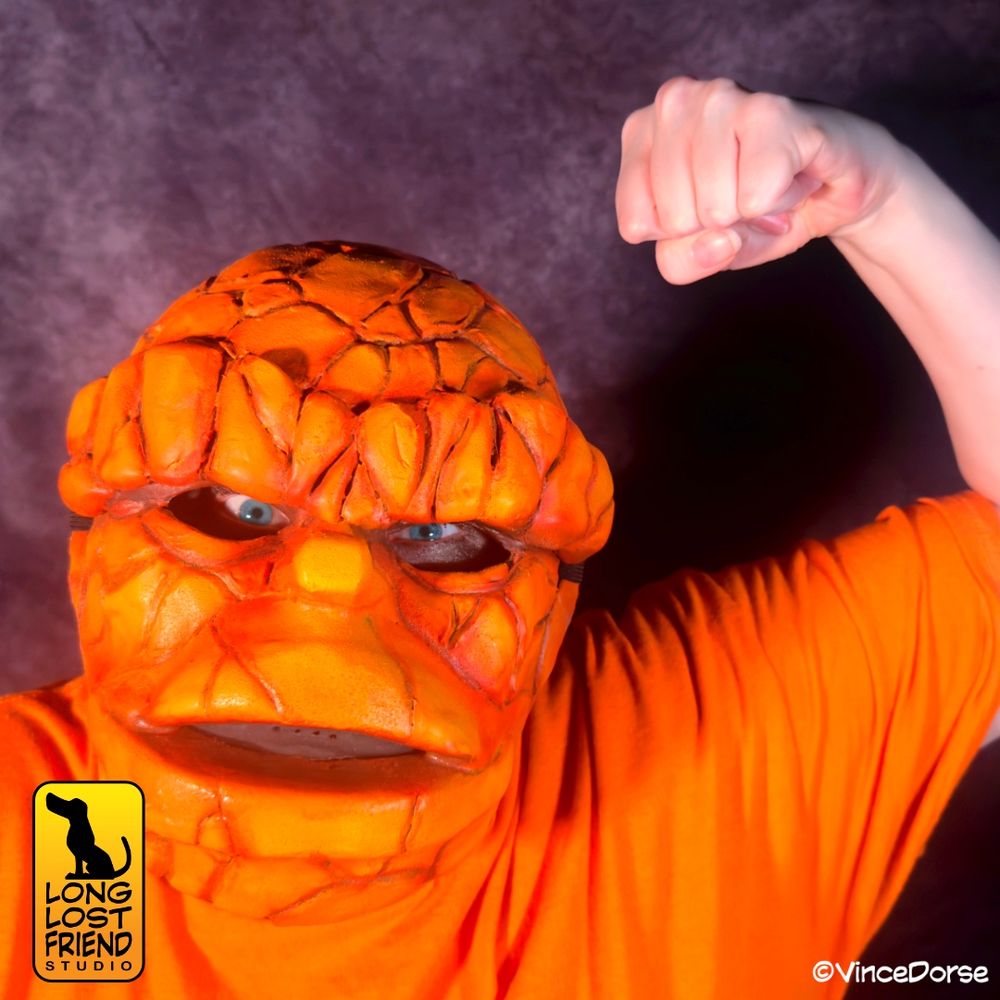 woman wearing a homemade Ben Grimm Thing mask, along with orange t-shirt, brandishing her fist like The Thing does in the comics