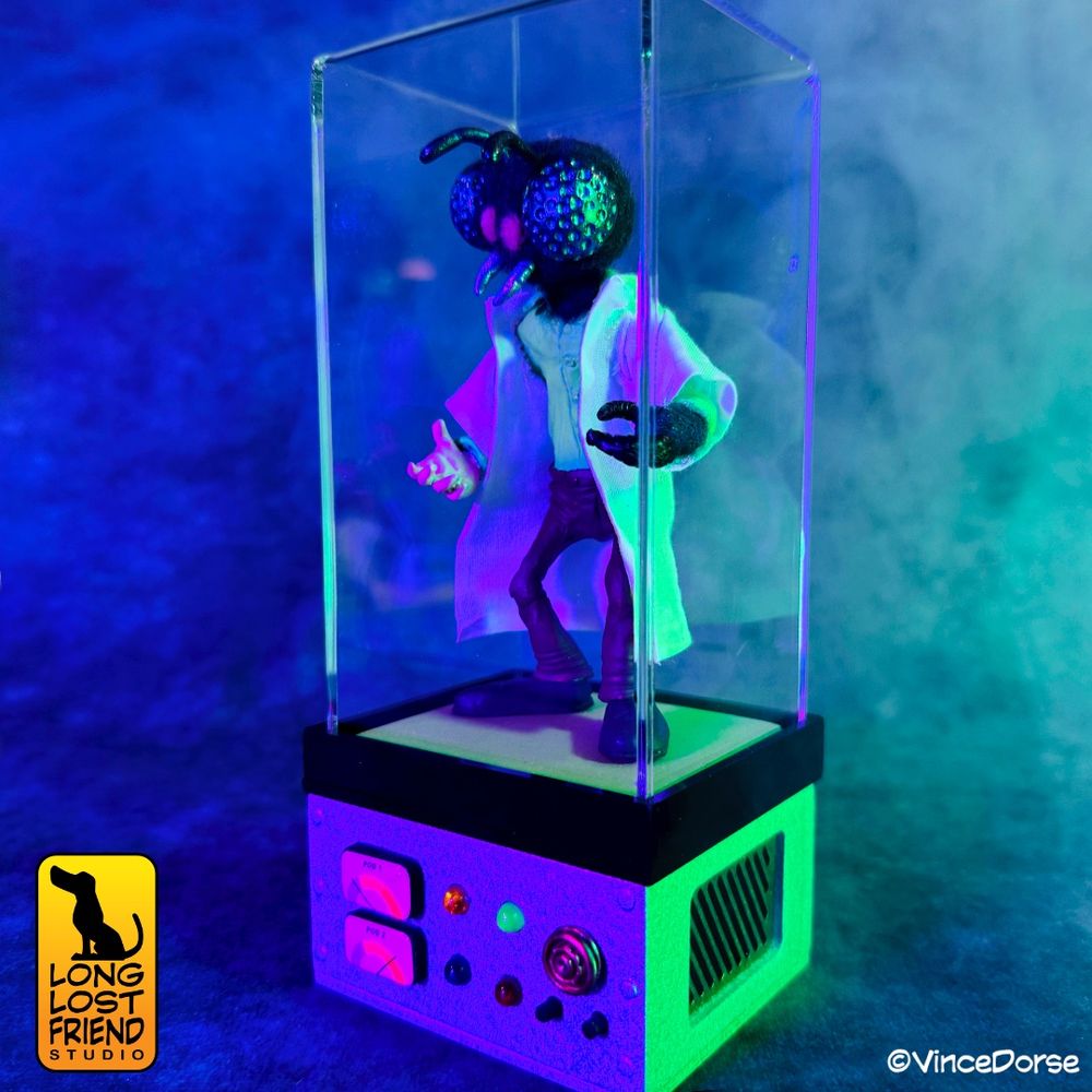 mixed-media diorama of a human fly in a lab coat, standing in a teleport chamber