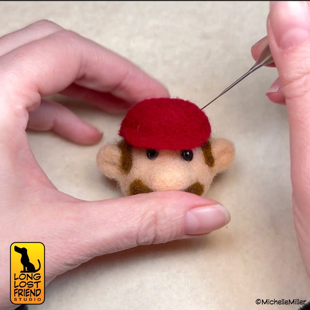 detail of the Mario needle felted head having his red hat felted on with a needle, the head is resting on a wool pad
