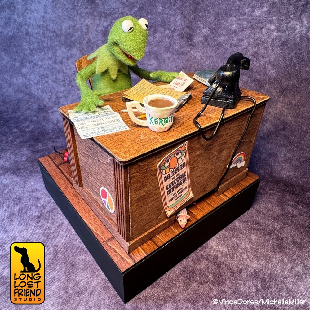 Kermit the Frog mixed media diorama.  Kermit is needle felted and is sitting at his desk. The desk and stage floor are made of wood. The telephone and mug are made of clay. There are various papers and books on the desk. Diorama made by Vince Dorse and Michelle Miller of Long Lost Friend Studio.