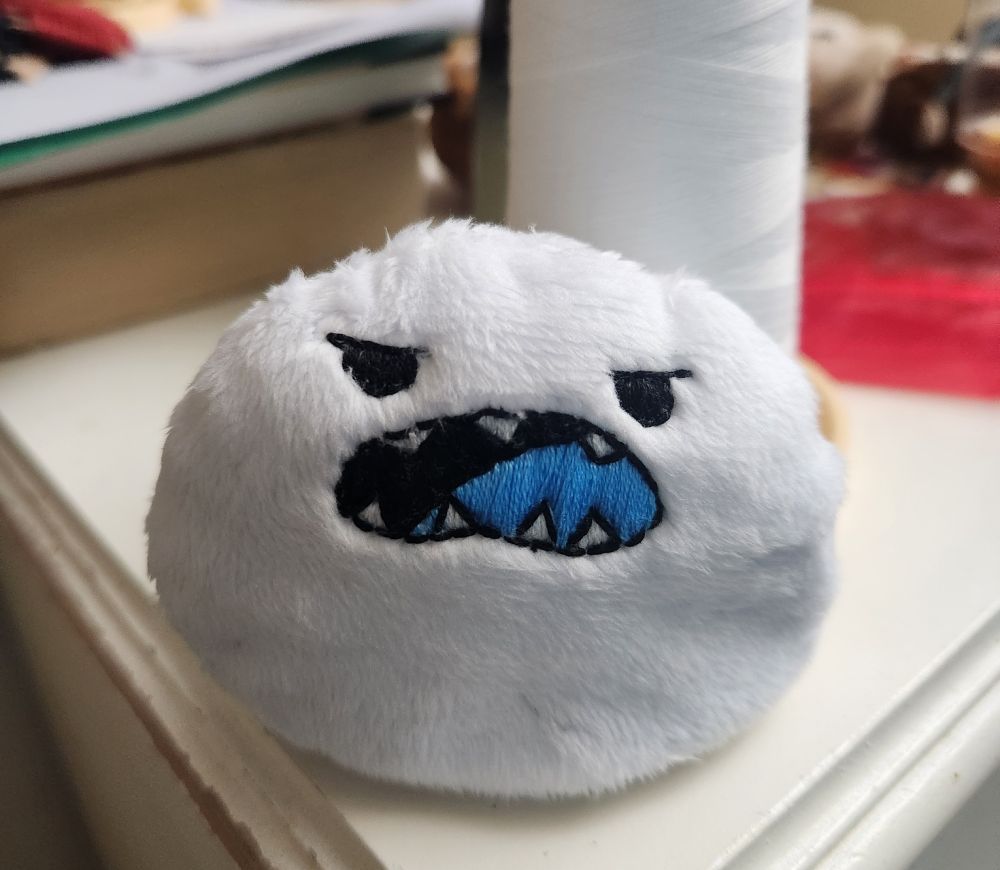 White puff ball plush of Langa’s Yeti with half lided eyes and an open mouth with blue tongue 