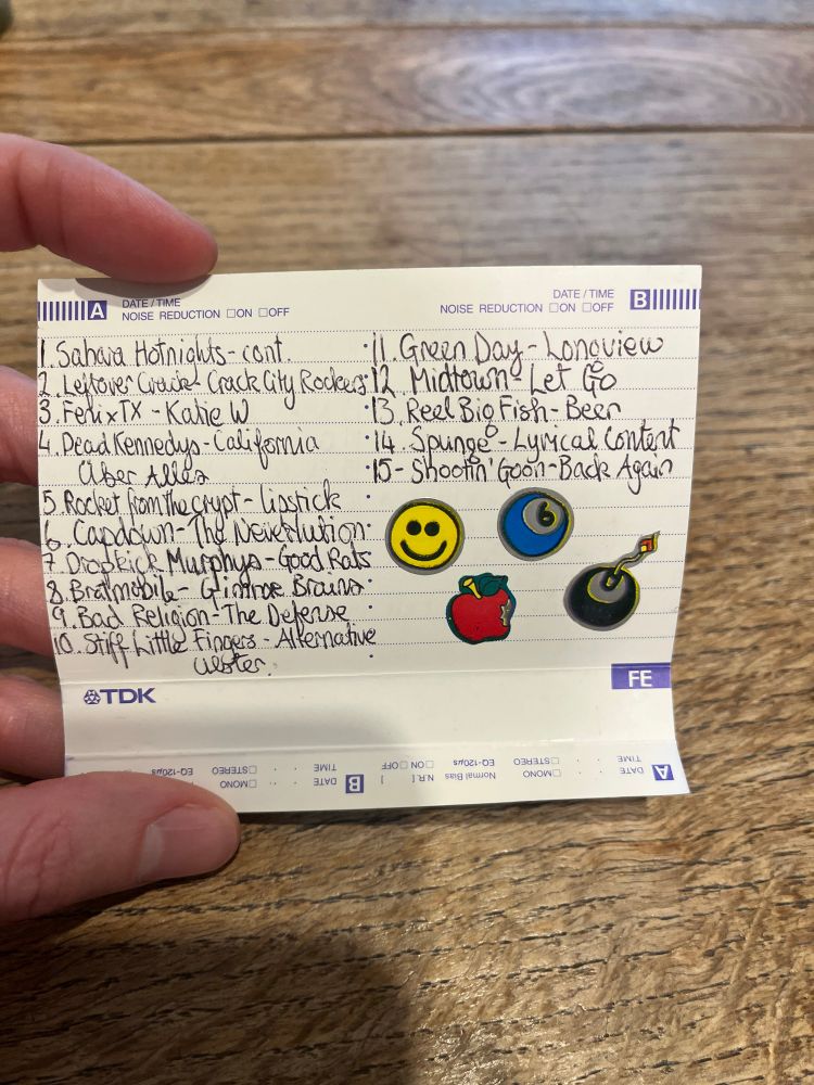The liner of a blank tape, decorated with stickers. In super tiny handwriting is a monumentally early 2000’s playlist that includes Dropkick Murphy’s, Fenix TX, and Bad Religion.