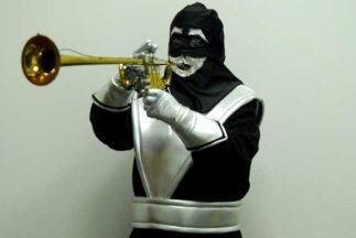 A photo of Chacal, a running character on Spanish-language television show Sábado gigante who wears a costume of black over their whole body and bands od silver across it's body, waist shoulders and marking their face. The character holds a brass horn.