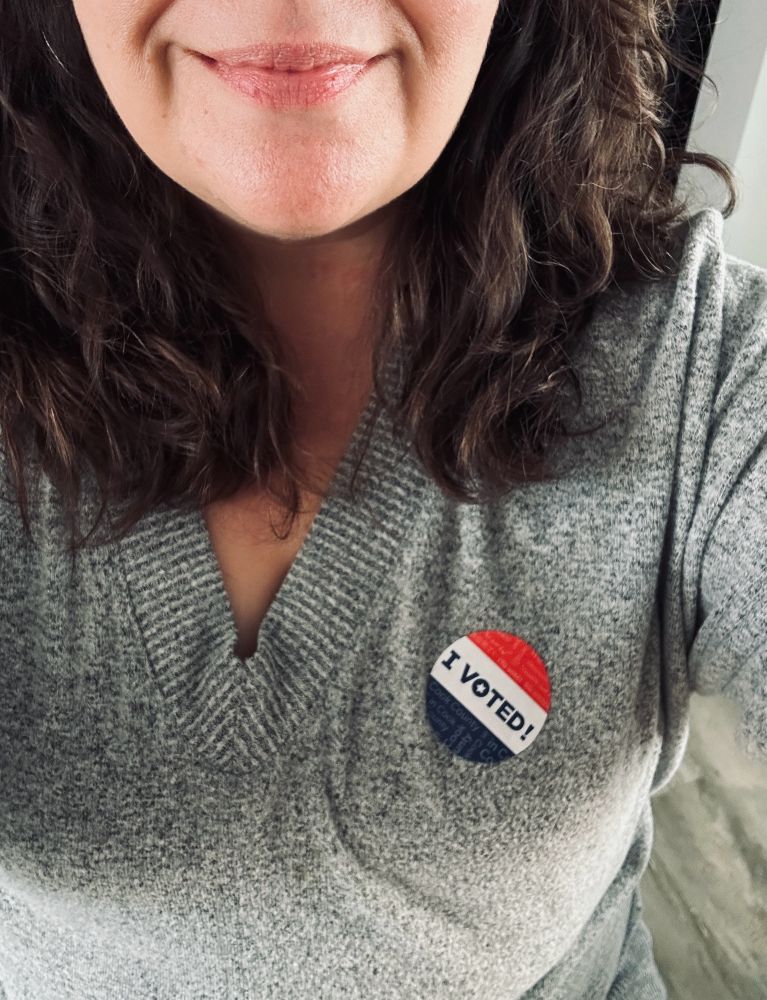 Me from the chin down in a grey shirt with a red, white, and blue "I voted" sticker