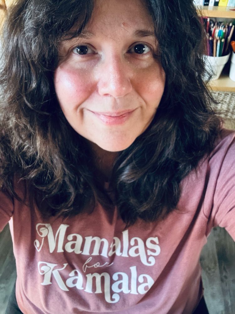 Me with brown over the shoulders hair and a slight smile wearing a pink "Mamalas for Kamala" tshirt