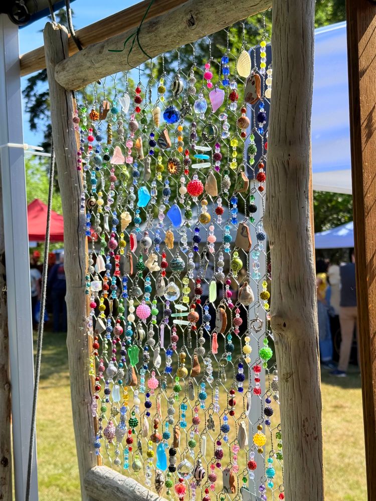 An artist’s colorful beach-styled bead collage with a light wooden frame. The sun behind the art creates a glow on the beads.