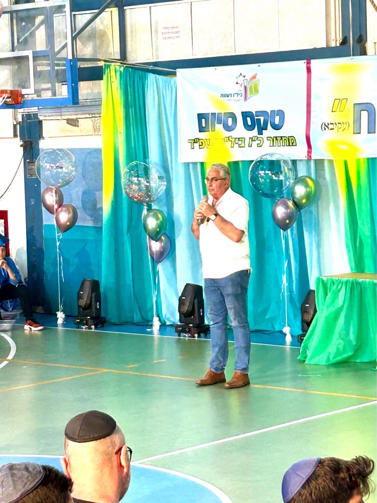 Ein Mann steht vor Ballons und buntem Vorhang mit Mikrofon in einer Turnhalle