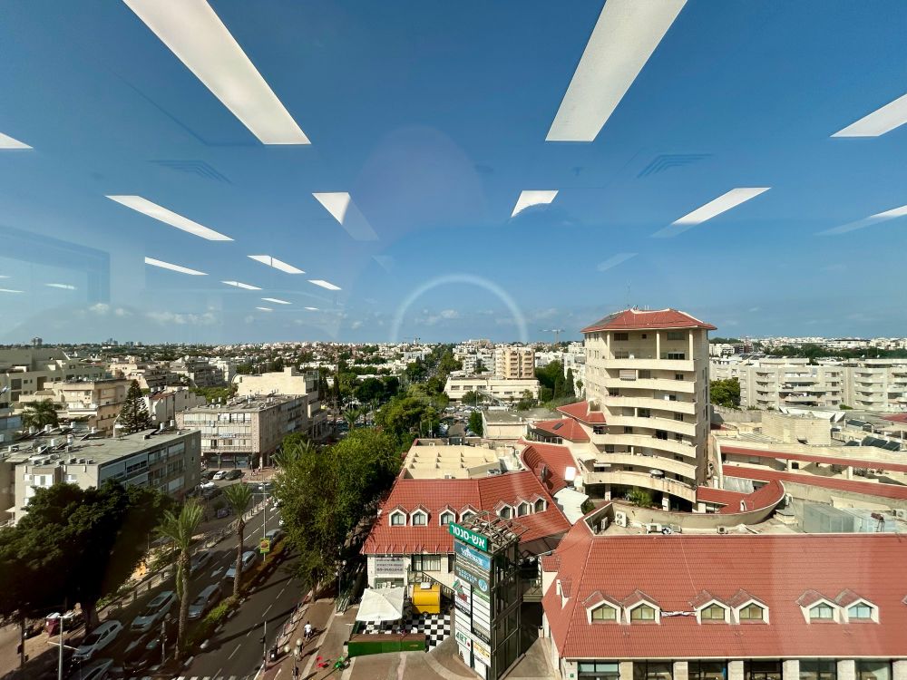 Blick auf eine Kleinstadt aus dem Fenster eines Büroturms. Die Deckenlampen spiegeln sich im Fenster und erzeugen eine Illusion von Lichtrechtecken im Himmel. 