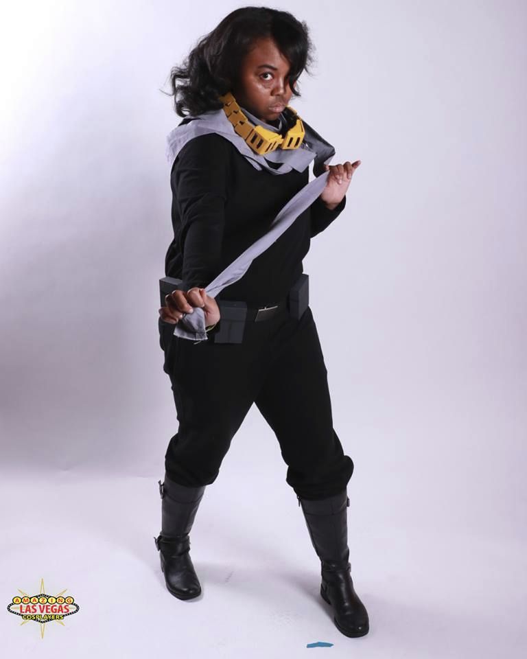 A photo of patchouliies dressed as Eraserhead/Aizawa Shouta from My Hero Academia, posed at a turn while holding a their long grey scarf out to the viewer. 