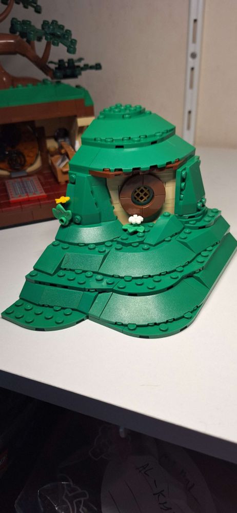 In Lego: The outside of bilbo's writing corner, a round window and some walls covered with grass.