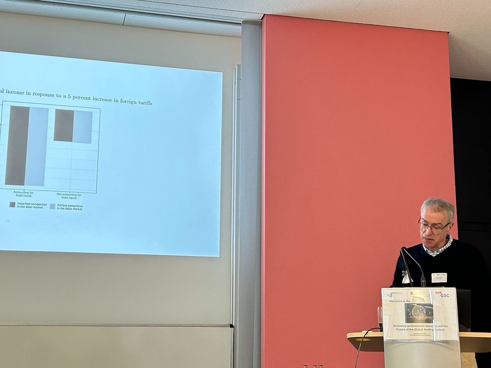 Professor Holger Görg of the Kiel Institute is seen infront of a chart projected to a screen discussing the presentation previously given.