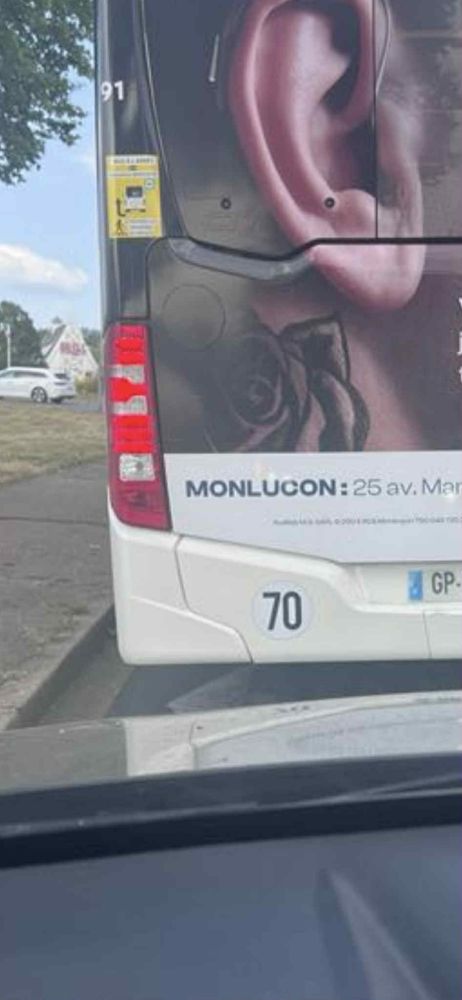 Une publicité Audika sur un bus avec une faute d'orthographe "Monlucon" au lieu de Montluçon. 
Environnement de ville avec le bus en second plan et notre voiture au premier plan.