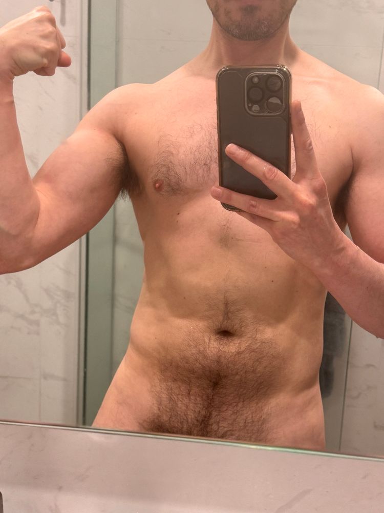 Headless torso, adifferentjon in a nude post-gym mirror selfie at home, slightly different pose, cropped portrait showing off arms day progress with a flexed bicep, short salt and pepper beard, light chest hair, and dense stomach hair with visible bush peeking out at the bottom of the mirror 