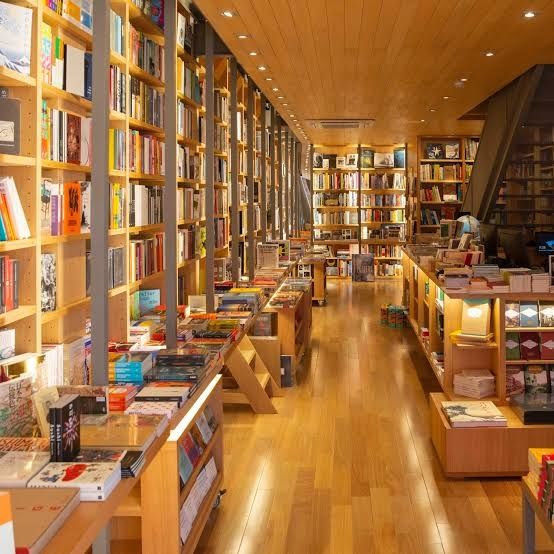 Livraria. Ambiente com piso e teto de madeira, diversas estantes iluminadas cheias de livros.