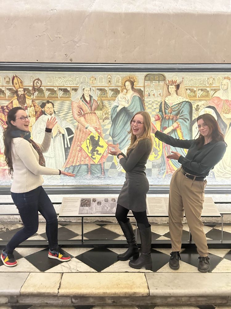 3 femmes qui posent en souriant et en ayant l'air contente devant une peinture murale de personnages médiévaux au musée de l'Hospice Comtesse à Lille