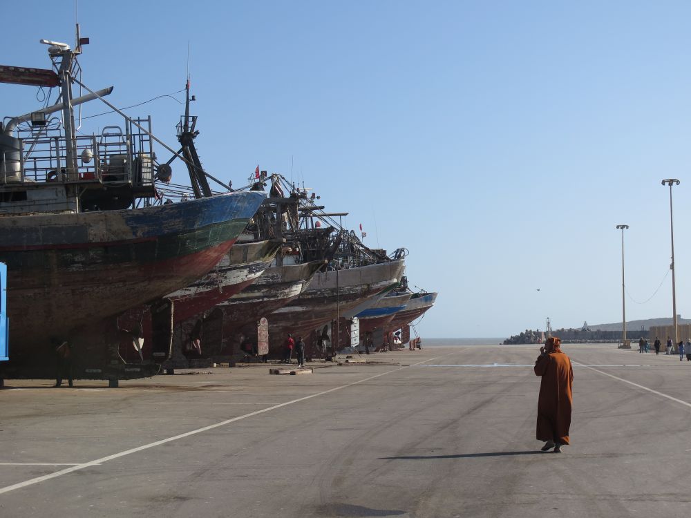photo du port d'Essaouira avec des bateaux de pêche à sec qui sèchent et un homme en djellaba marron qui les regarde