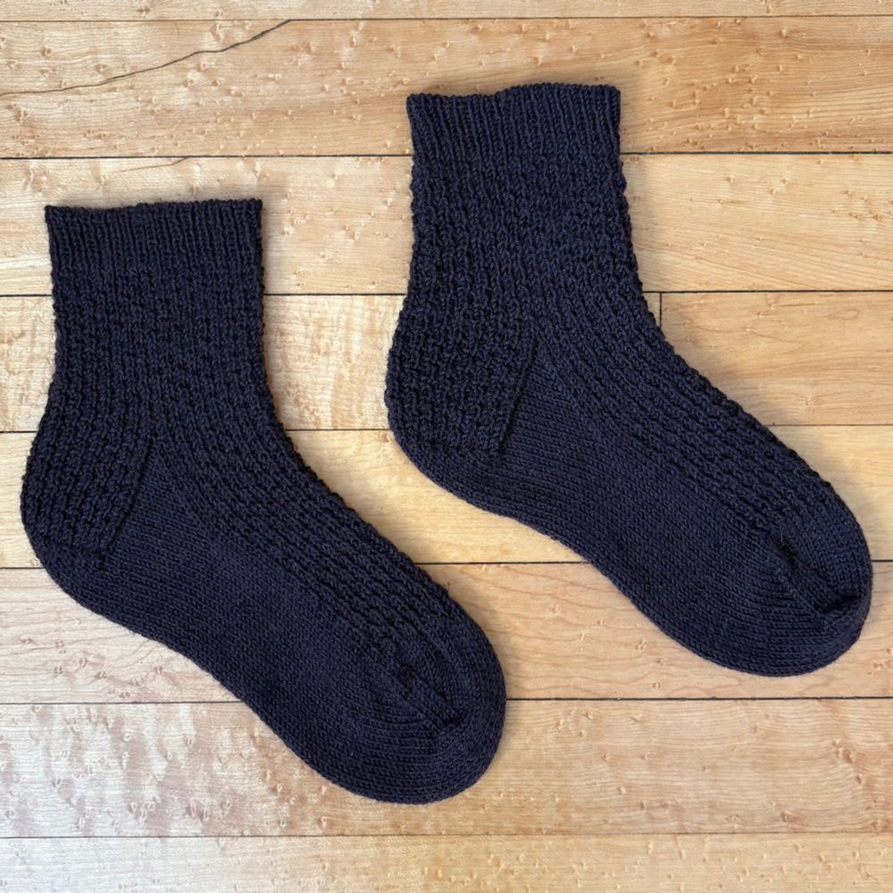 A pair of handknit socks with each sock laid out side by side fresh off the sock blockers.