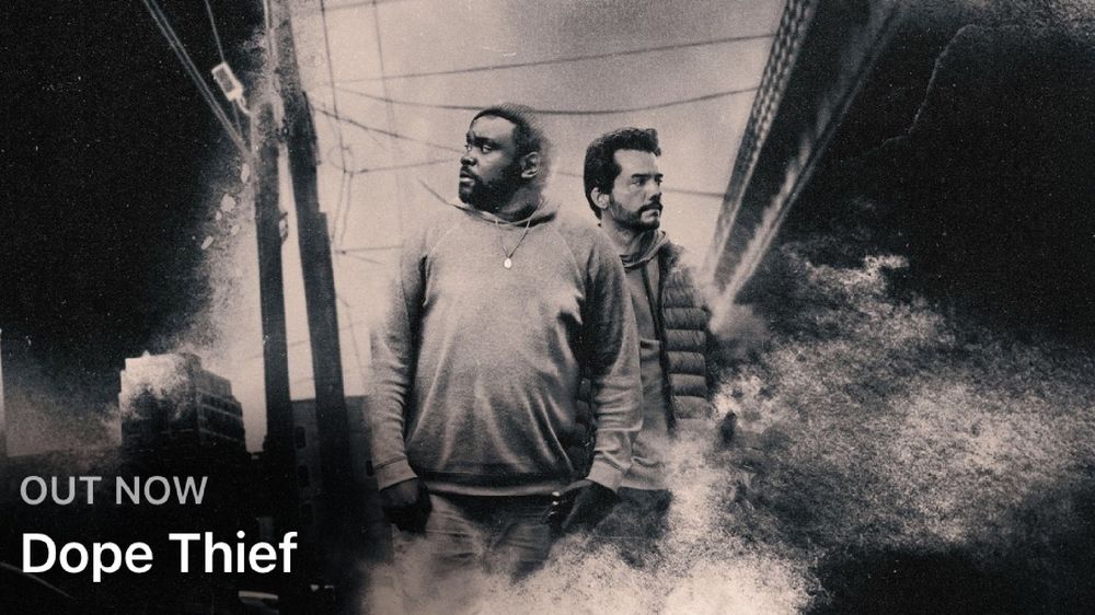 Ein Schwarz-Weiß-Werbebild für "Dope Thief", mit zwei Männern, die nebeneinander stehen, mit einem Hauch von urbanem Hintergrund und atmosphärischen Effekten. Der Text unten zeigt an, dass es jetzt verfügbar ist.