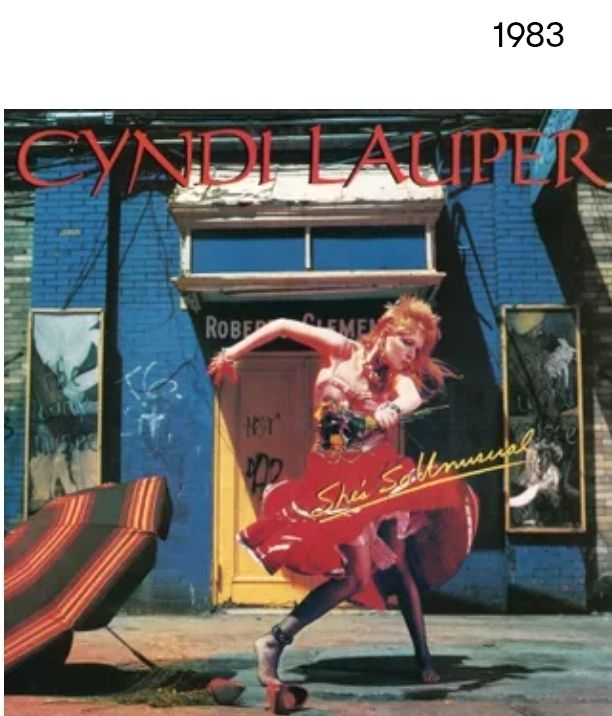 1983 - Cyndi Lauper She's So Unusual album cover - Cyndi dancing in the street with bright orange hair, colorful busier, red petticoat, fishnets and bare feet