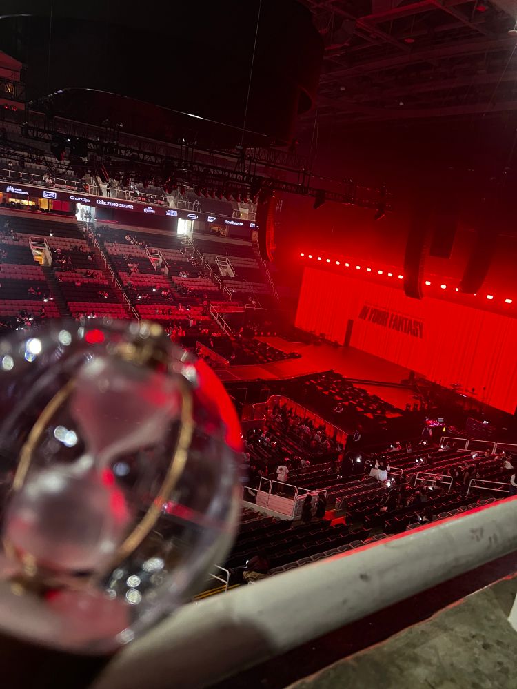 A photo with an ATEEZ lightstick in the foreground and the stage dressing for the concert in the background as a giant (digital) red curtain