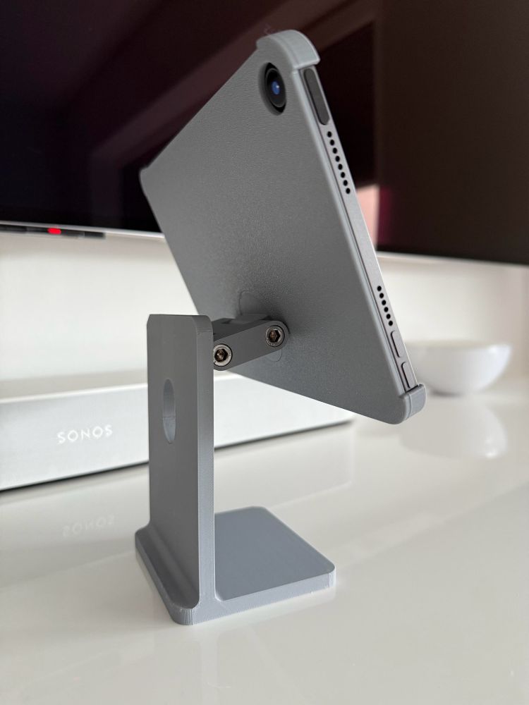 iPad mini in a grey 3D printed holder that looks like a Apple Studio Display stand. It’s standing on a white table. Shown from the back.

The stand shows a two-point hinge that enables the iPad to move in different angles.