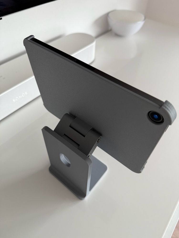 iPad mini in a grey 3D printed holder that looks like a Apple Studio Display stand. It’s standing on a white table. Shown from the top back.

The stand shows a two-point hinge that enables the iPad to move in different angles.